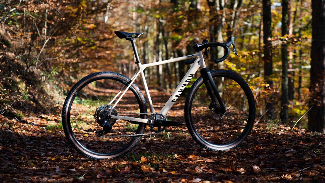 Canyon gravel bike with wide tire clearance for rugged trails, shown in a serene forest setting during fall