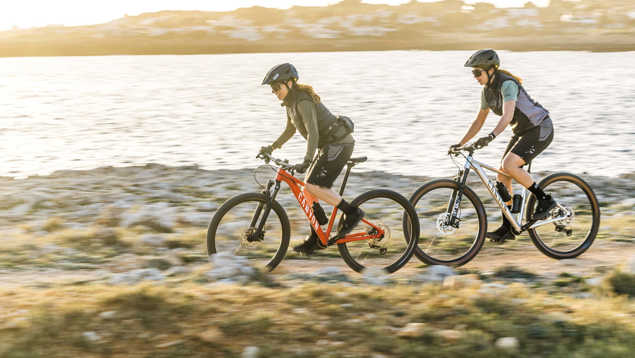 Two cyclists riding Grand Canyon hardtail mountain bikes along a coastal trail at sunse