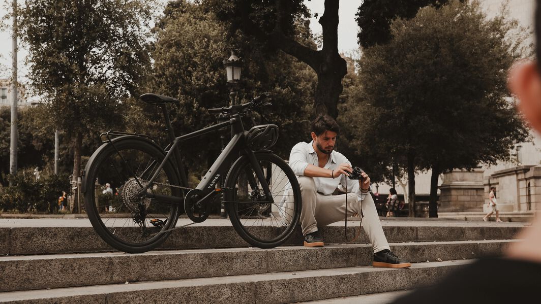 Man sitting on stone steps beside a Canyon bike, adjusting his camera in a park setting.