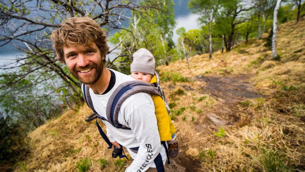 Max Schumann carries a baby on his back as he hikes up a mountain.